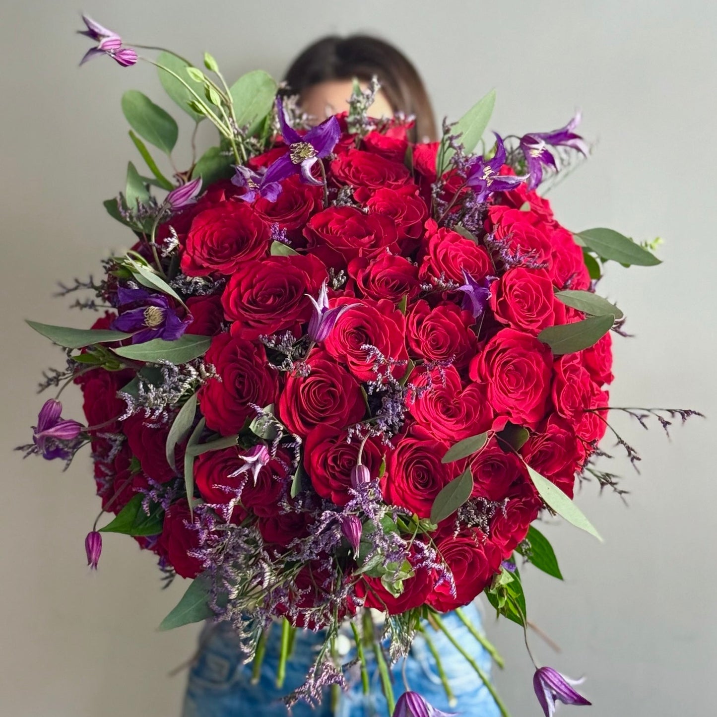 Person holding a big red bouquet on grey background 