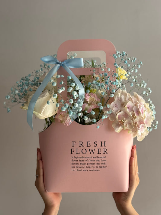 Pink box with flowers and a blue bow held by hands against a plain background