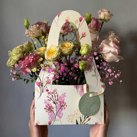 Floral arrangement in a decorative box held by hands against a gray background