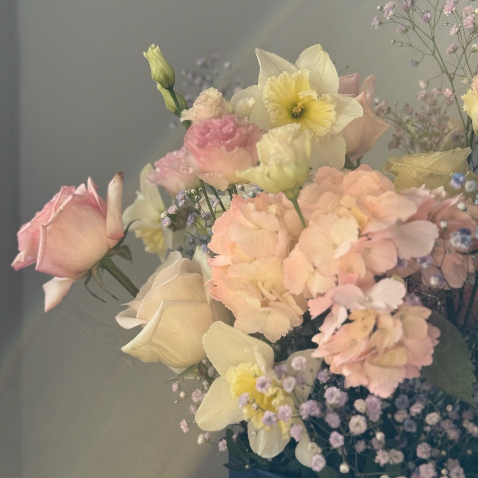 Bouquet of pastel flowers in a blue container against a gray background