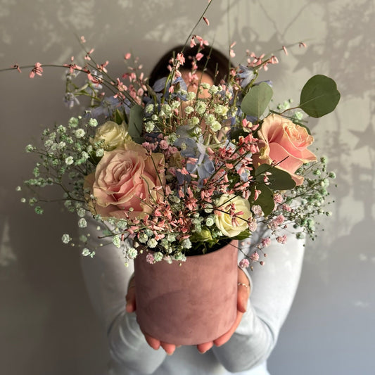 Person holding a bouquet of flowers in a pink vase against a neutral background