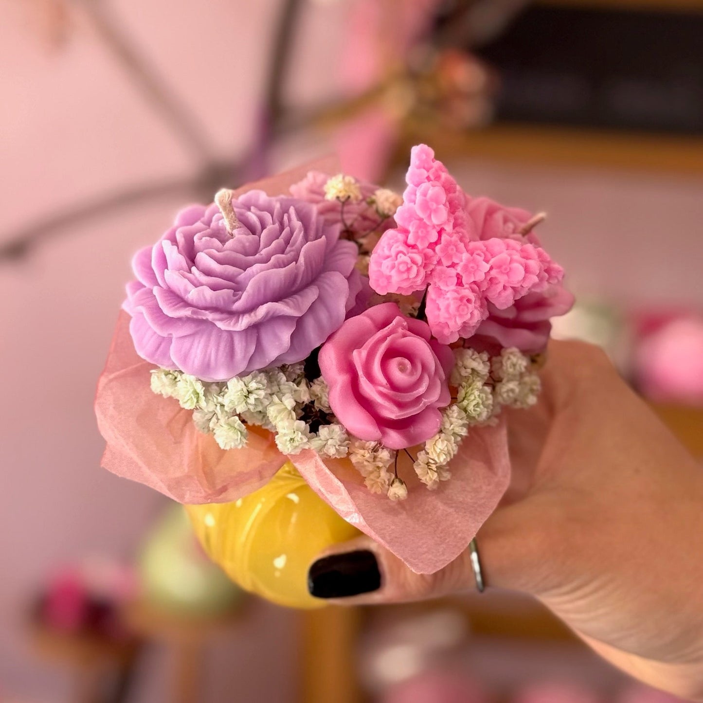 Decorative flower arrangement on a yellow cup held by a hand with a blurred background