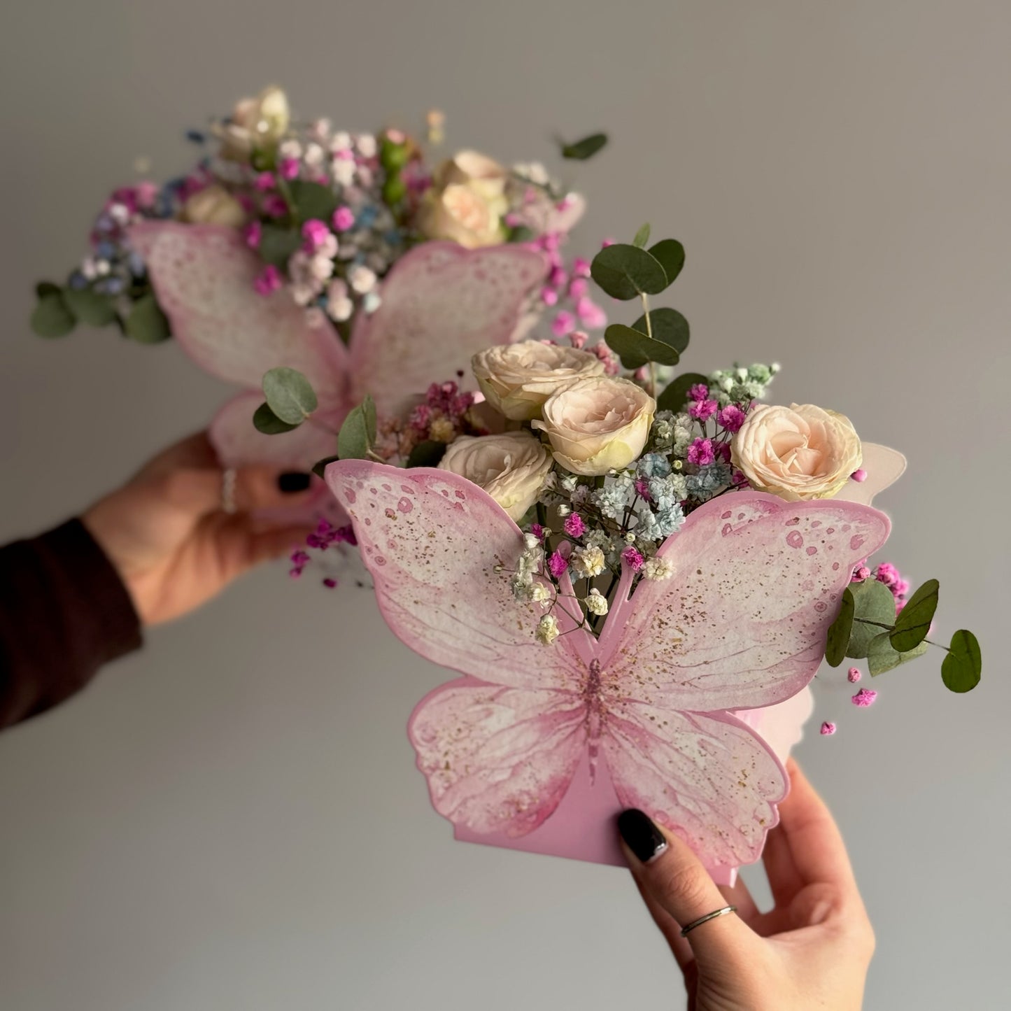 Bouquet of flowers with pink butterfly decorations held by hands against a neutral background