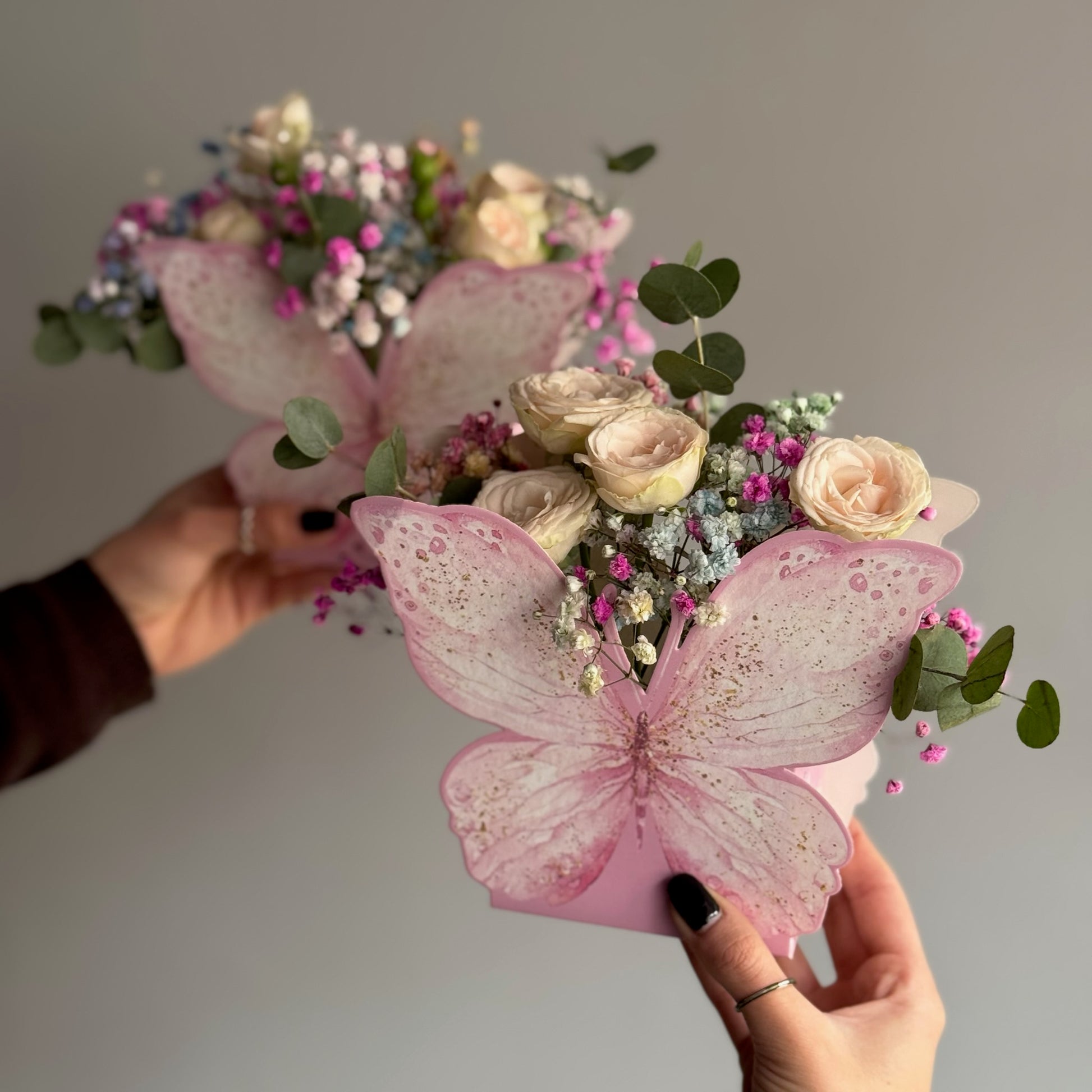 Bouquet of flowers with pink butterfly decorations held by hands against a neutral background
