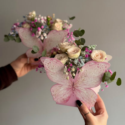 Bouquet of flowers with pink butterfly decorations held by hands against a neutral background
