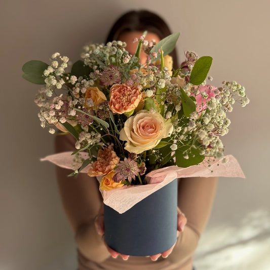 Person holding a bouquet of flowers wrapped in pink paper against a neutral background