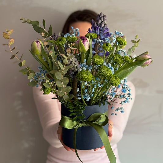 Person holding a bouquet of flowers in front of their face against a plain background