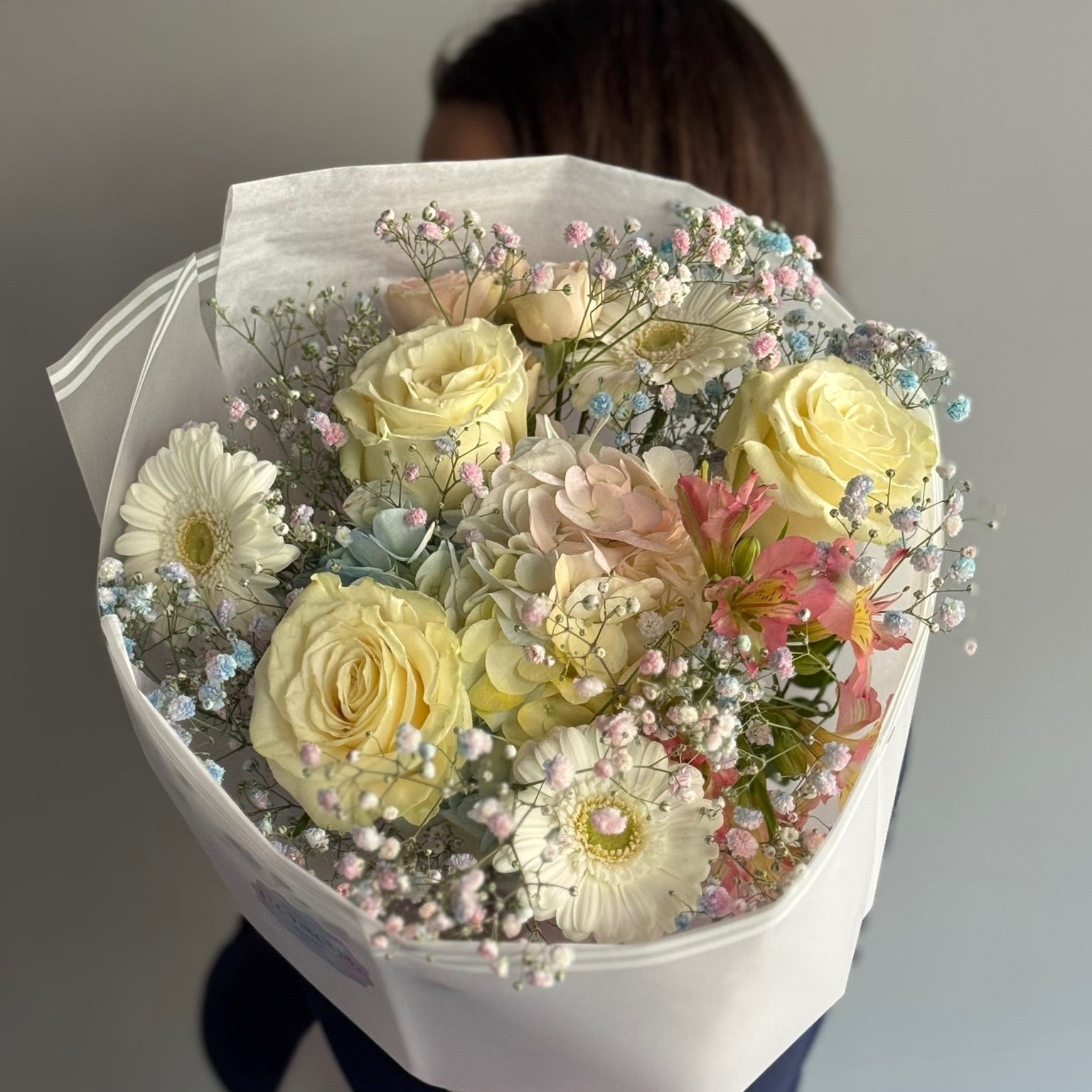 Bouquet of pastel-colored flowers held by a person against a neutral background