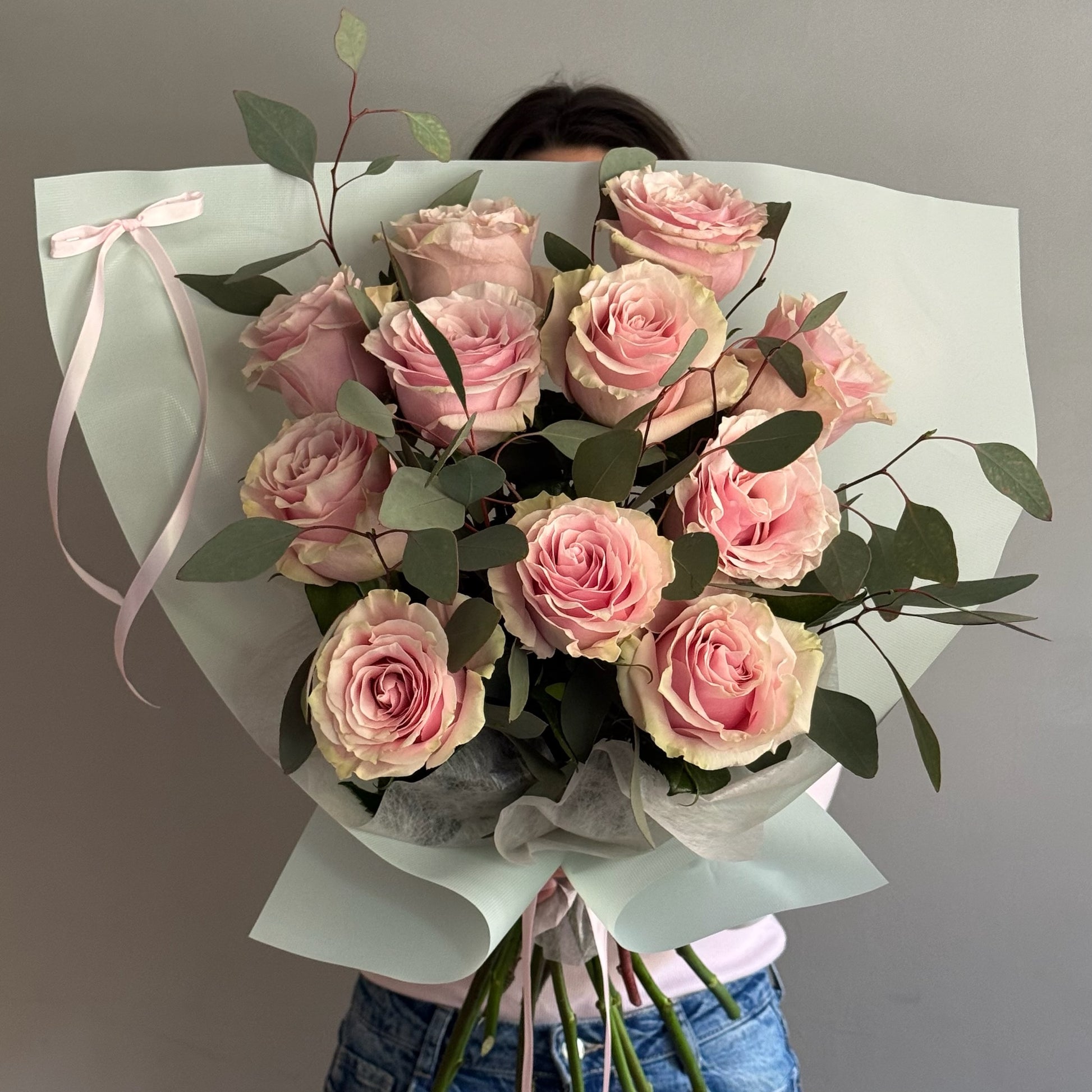 Bouquet of pink flowers wrapped in paper held by a person against a gray background