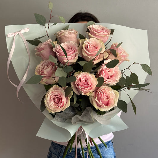 Bouquet of pink flowers wrapped in paper held by a person against a gray background