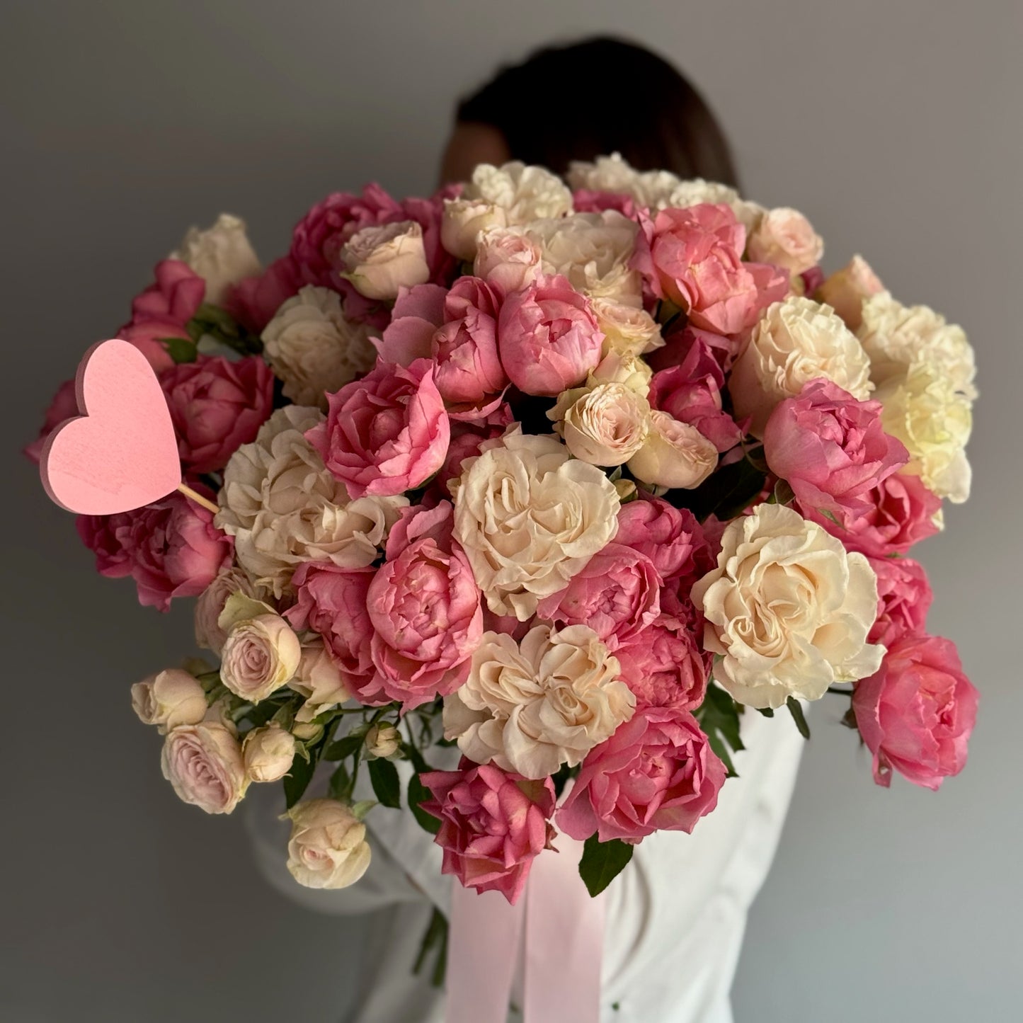Bouquet of pink and white roses with a heart-shaped balloon held by a person against a gray background