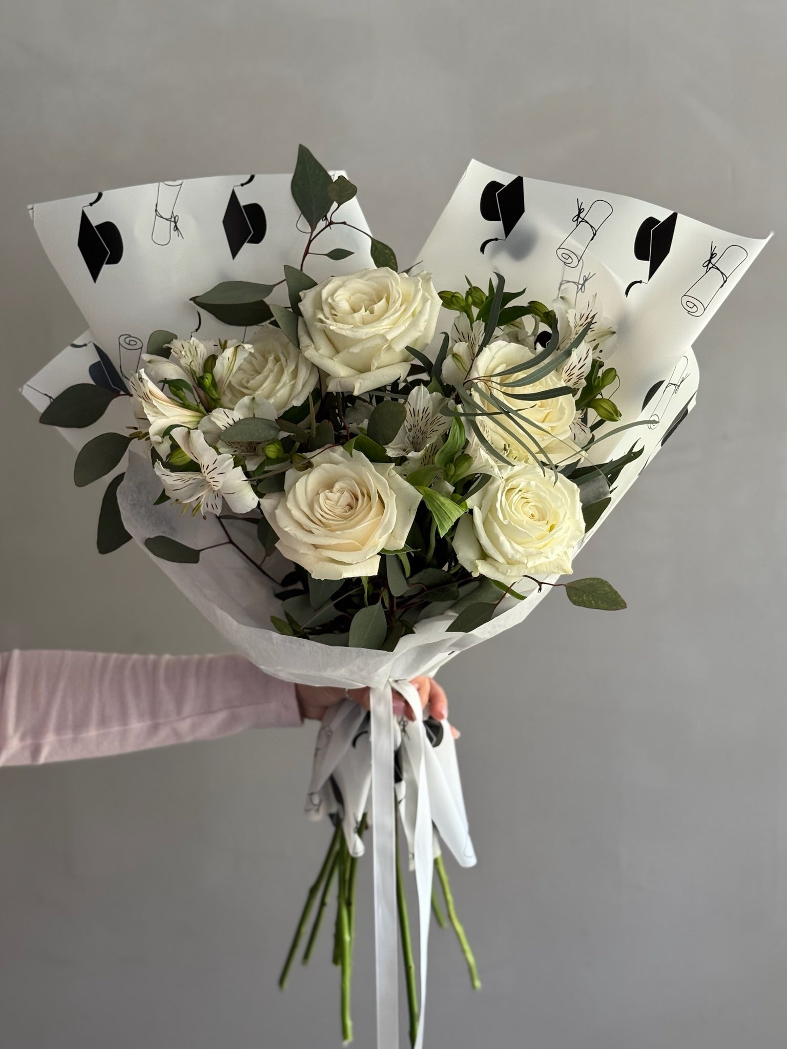 Bouquet with white flowers and graduation wrapping on grey background 