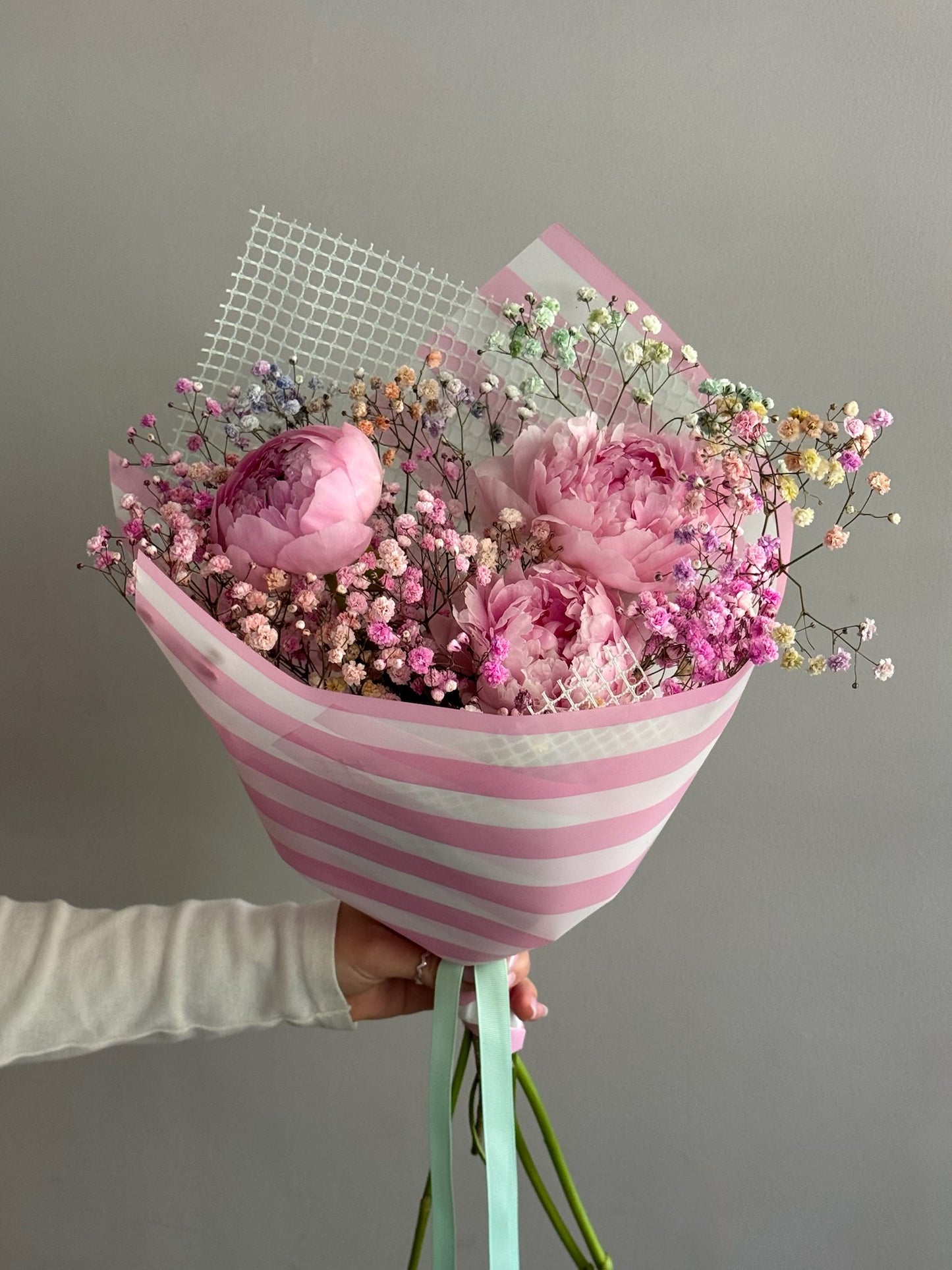 Pink peonies bouquet with pink stripes wrapping paper on grey background 