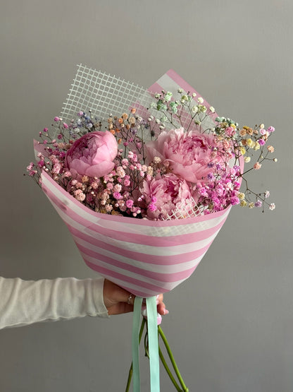 Pink peonies bouquet with pink stripes wrapping paper on grey background 