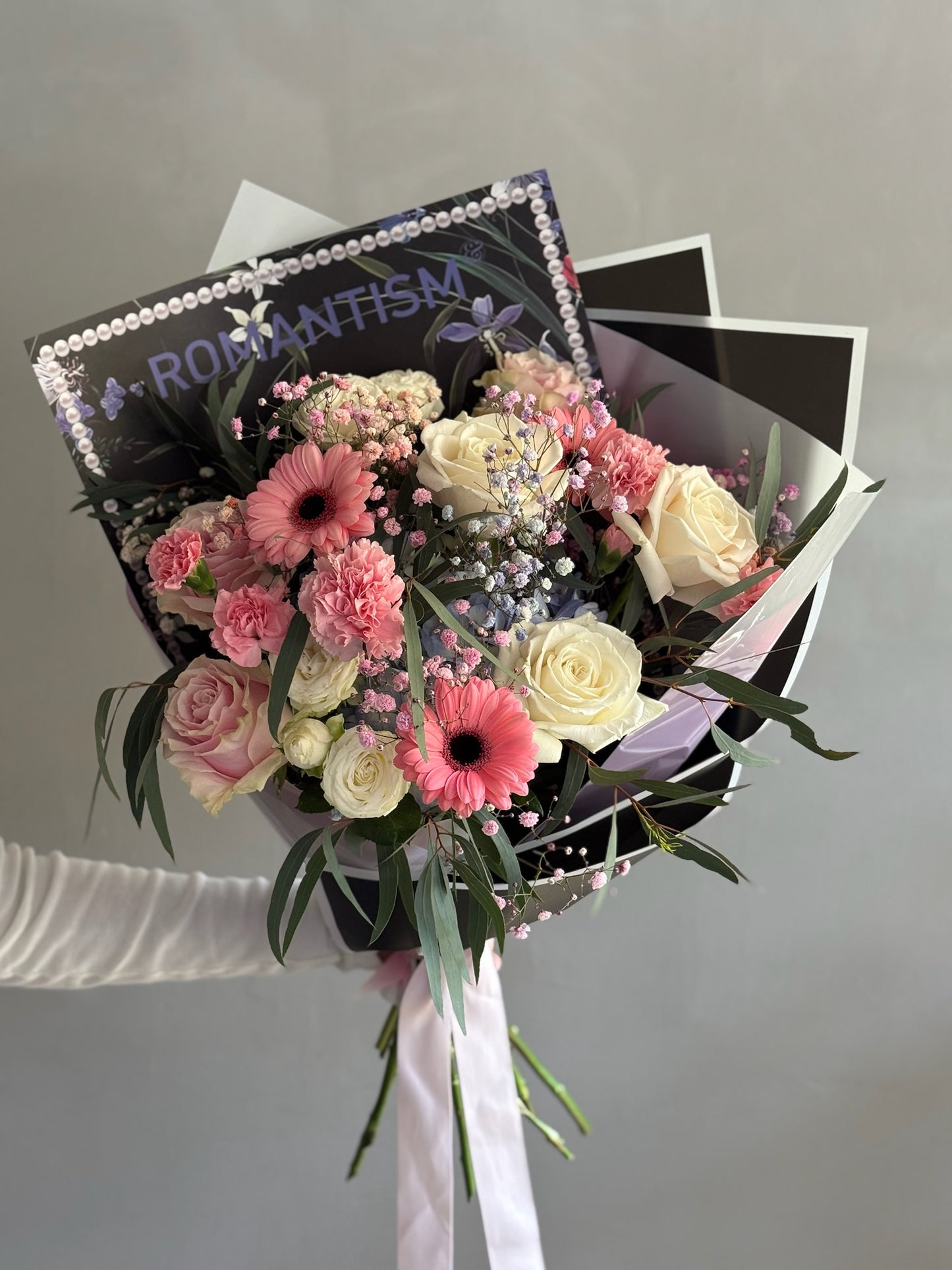 Pink bouquet with black wrapping paper on grey background 