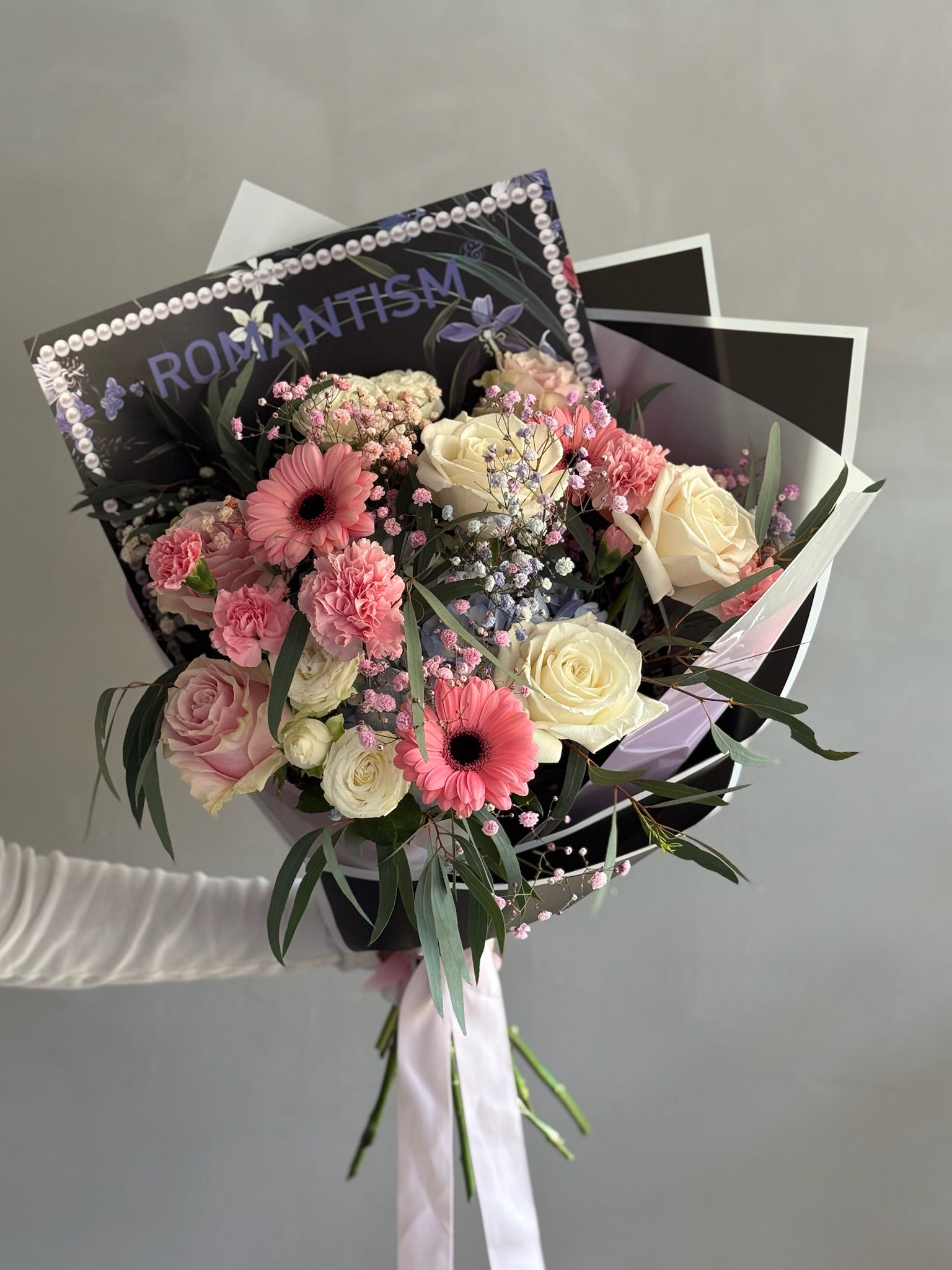 Pink bouquet with black wrapping paper on grey background 