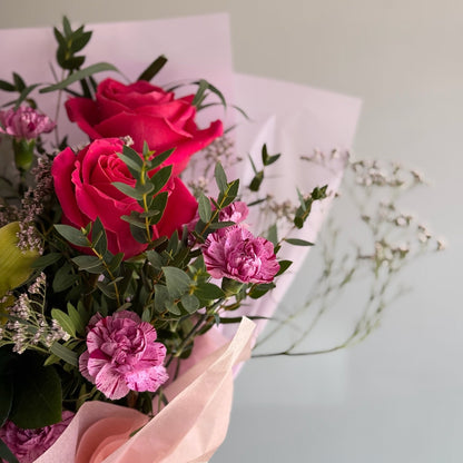 Bouquet of red and pink roses with greenery on a light background