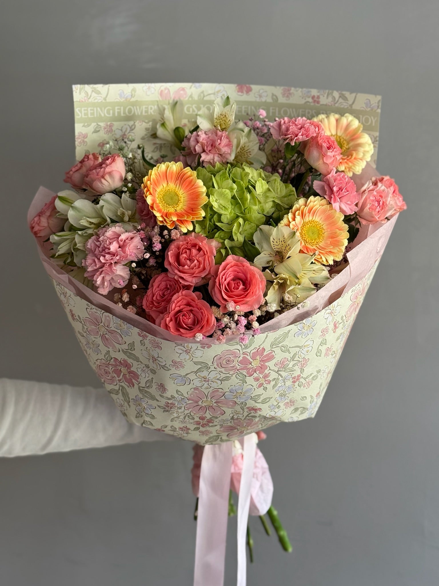 Colorful bouquet with mix of flowers in floral wrapping paper on grey background 