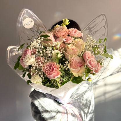 Bouquet of pink and white roses with butterfly wings packaging on a neutral background