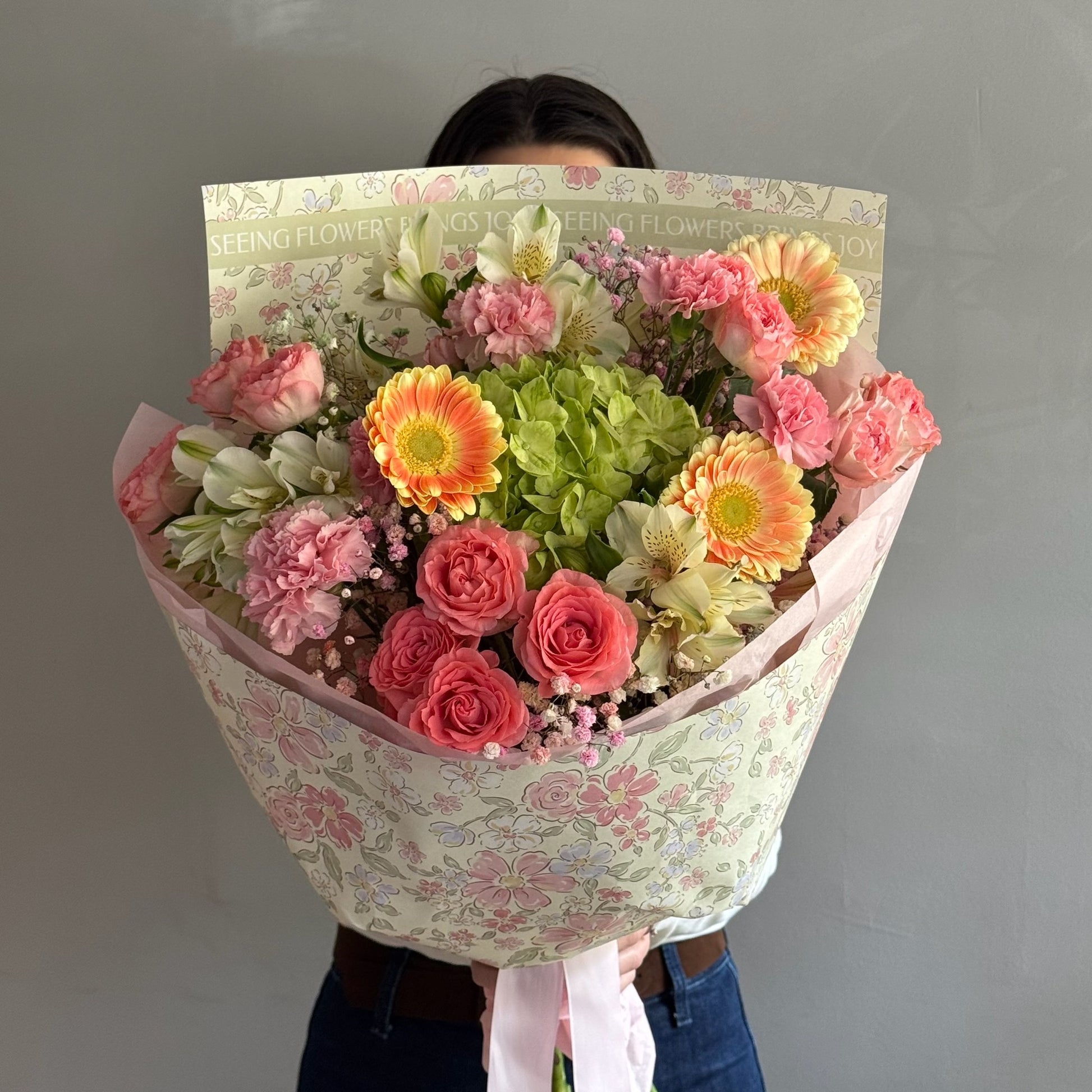 Colorful bouquet with mix of flowers and wrapping paper held on grey background 