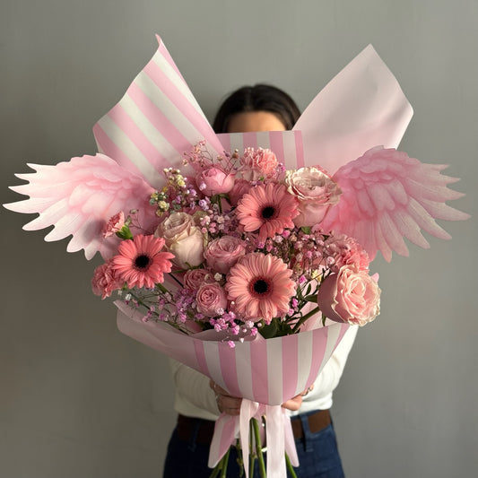 Pink Bouquet with pink flowers and wrapping paper held by person on grey background 