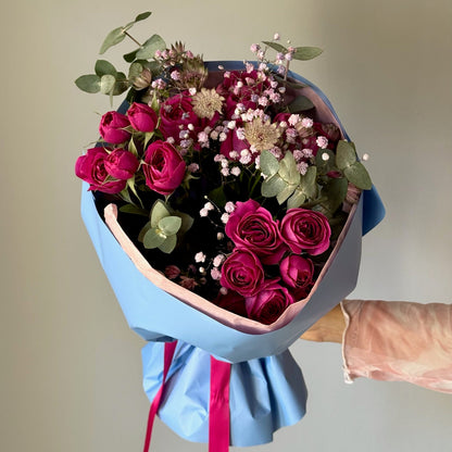 Bouquet of pink roses and greenery held by a person with a neutral background