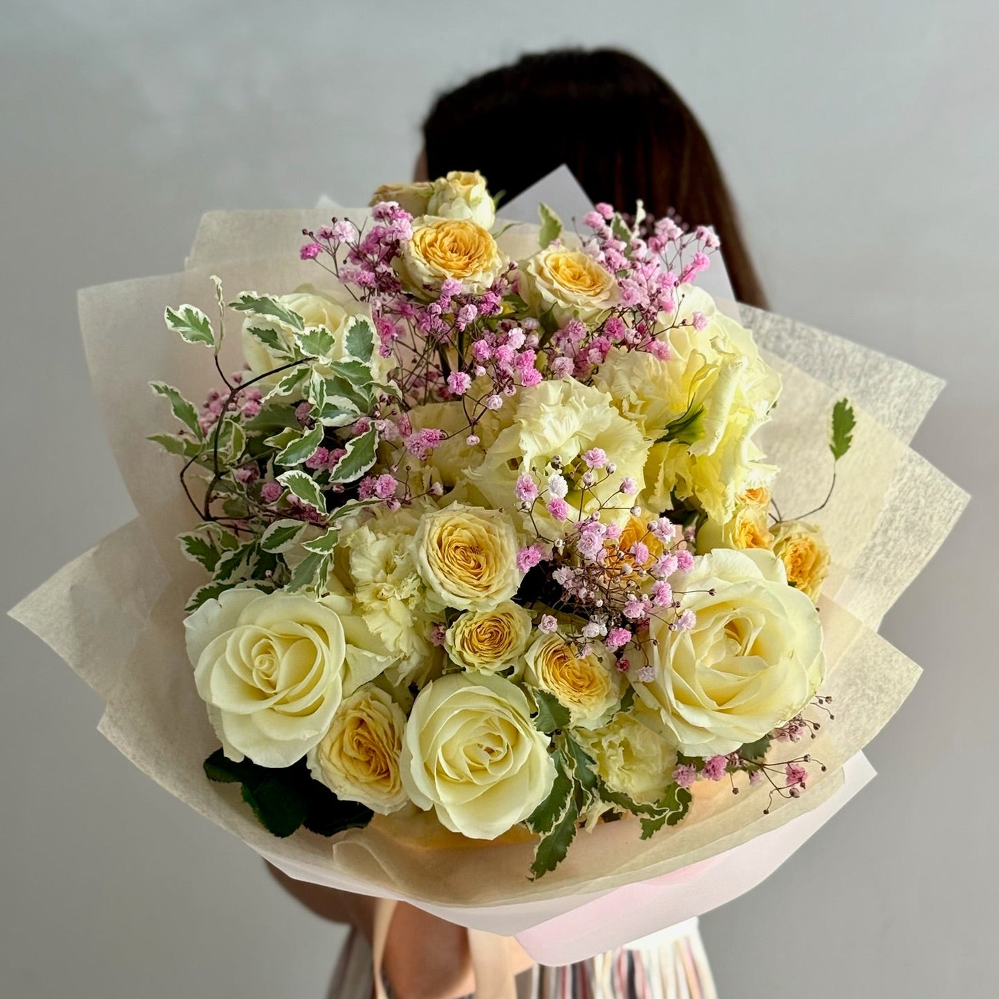Bouquet of yellow and white roses with greenery held by a person against a plain background