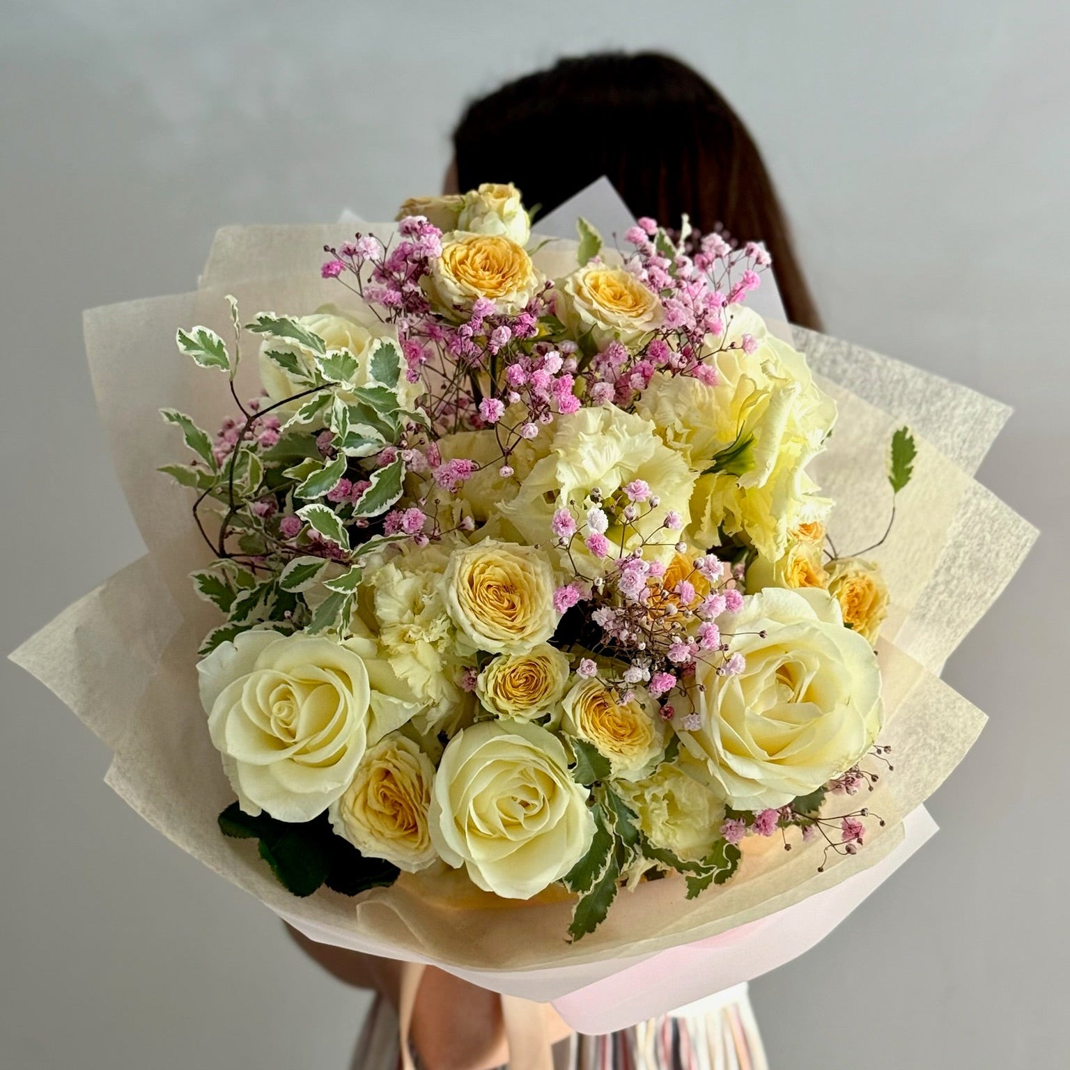 Bouquet of yellow and white roses with greenery held by a person against a plain background