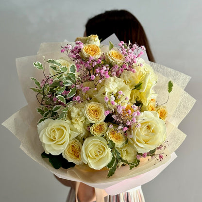 Bouquet of yellow and white roses with greenery held by a person against a plain background