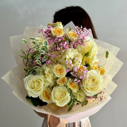 Bouquet of yellow and white roses with greenery held by a person against a plain background