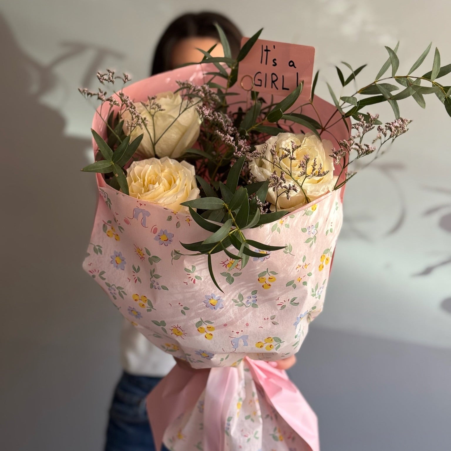 Bouquet of flowers wrapped in pink paper with a 'It's a Girl' sign held by a person.