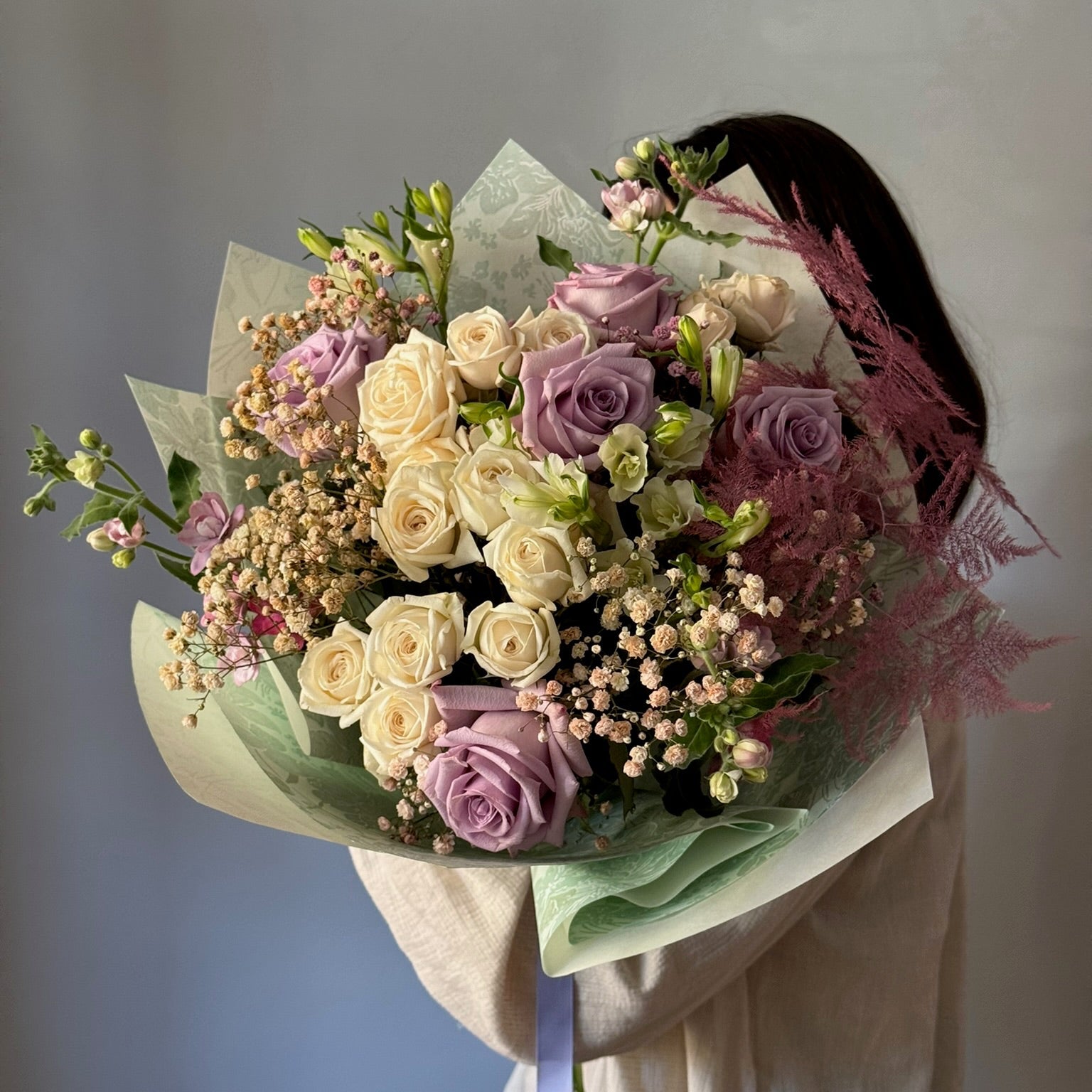 Person holding big white and purple bouquet on grey background 