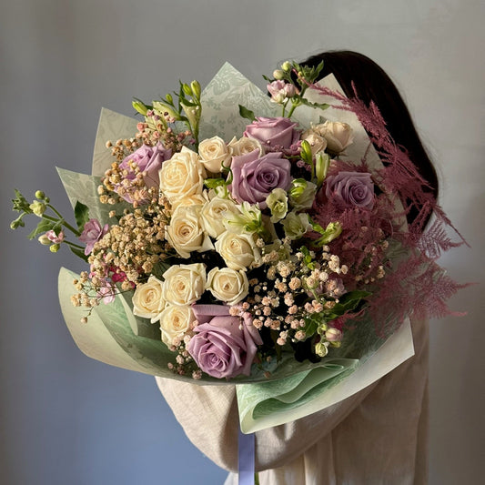 Person holding big white and purple bouquet on grey background 