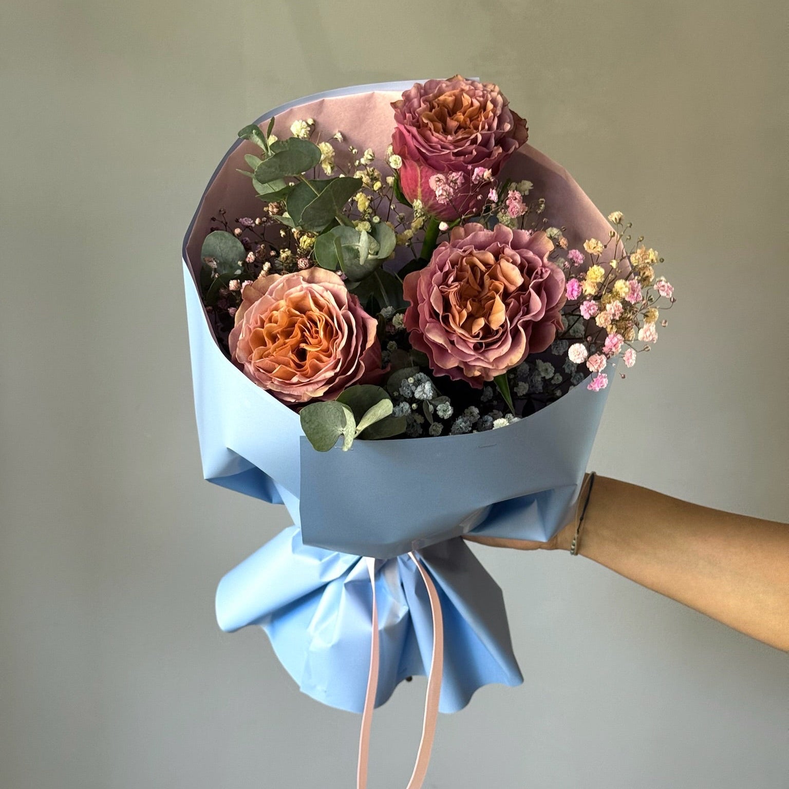 Bouquet of flowers wrapped in blue paper held against a plain background
