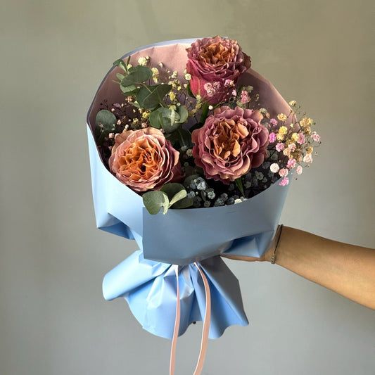 Bouquet of flowers wrapped in blue paper held against a plain background