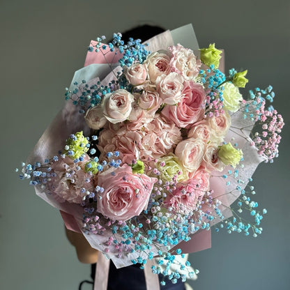 Bouquet of pink and white flowers with green and blue accents held against a neutral background