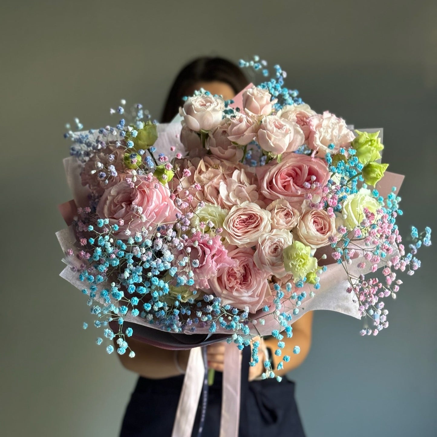 Bouquet of pink and white flowers with green accents held by a person against a plain background