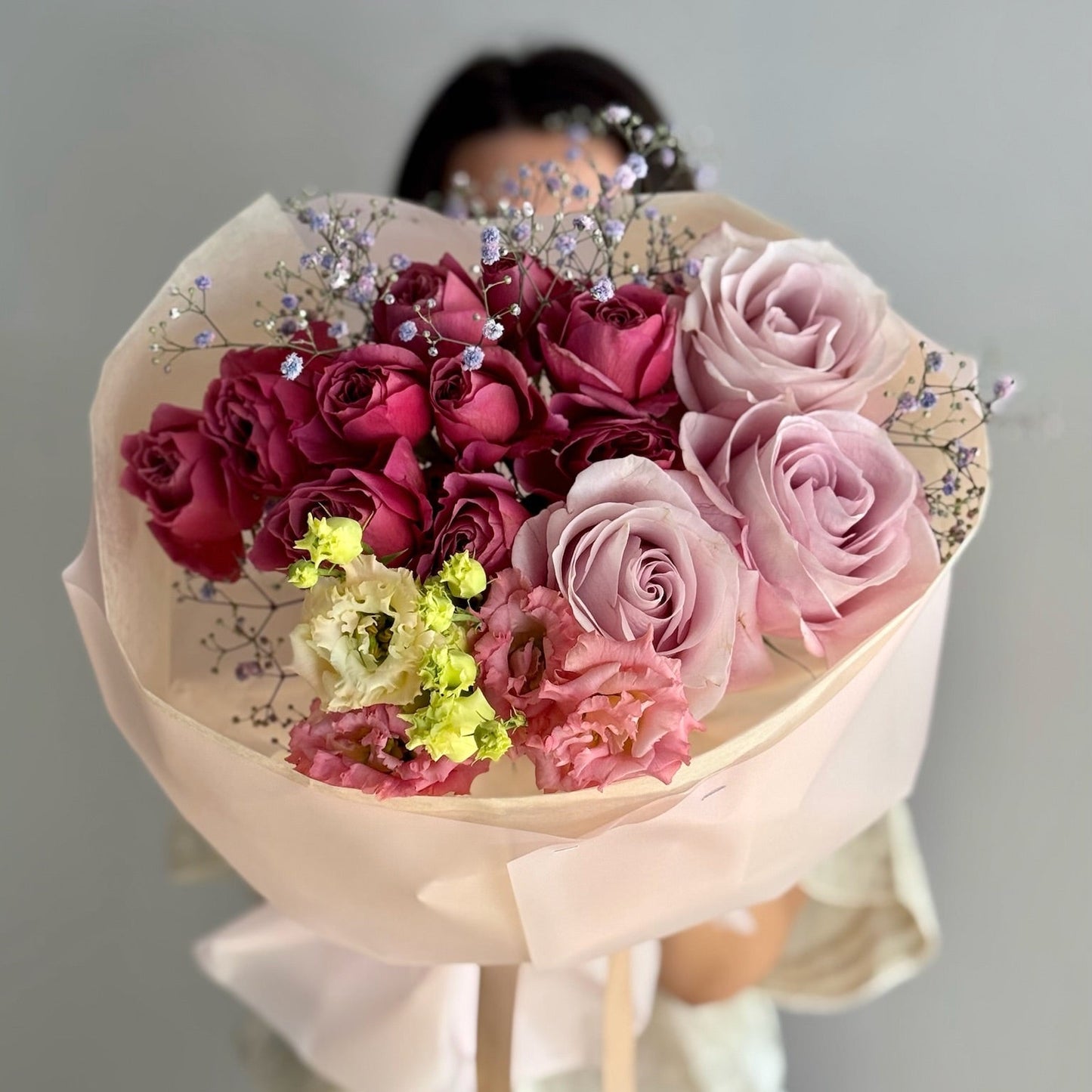 Bouquet of pink and red roses with decorative elements held by a person against a neutral background