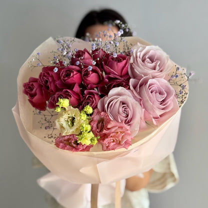 Bouquet of pink and red roses with decorative elements held by a person against a neutral background