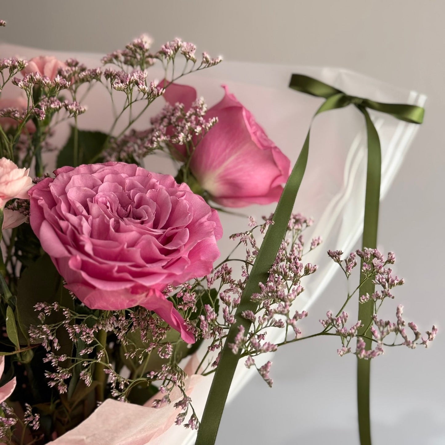 Bouquet of pink roses with a green ribbon on a light gray background