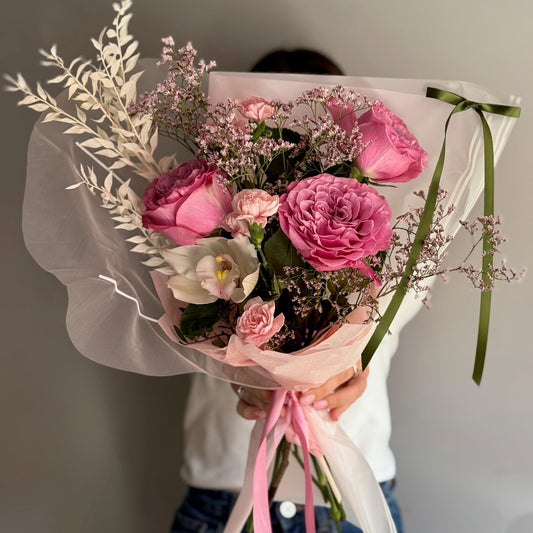 Bouquet of pink flowers with greenery held by a person against a neutral background