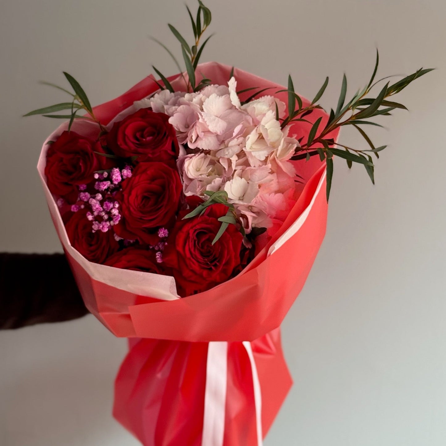 Bouquet of red and pink flowers wrapped in red paper with a white ribbon on a light background