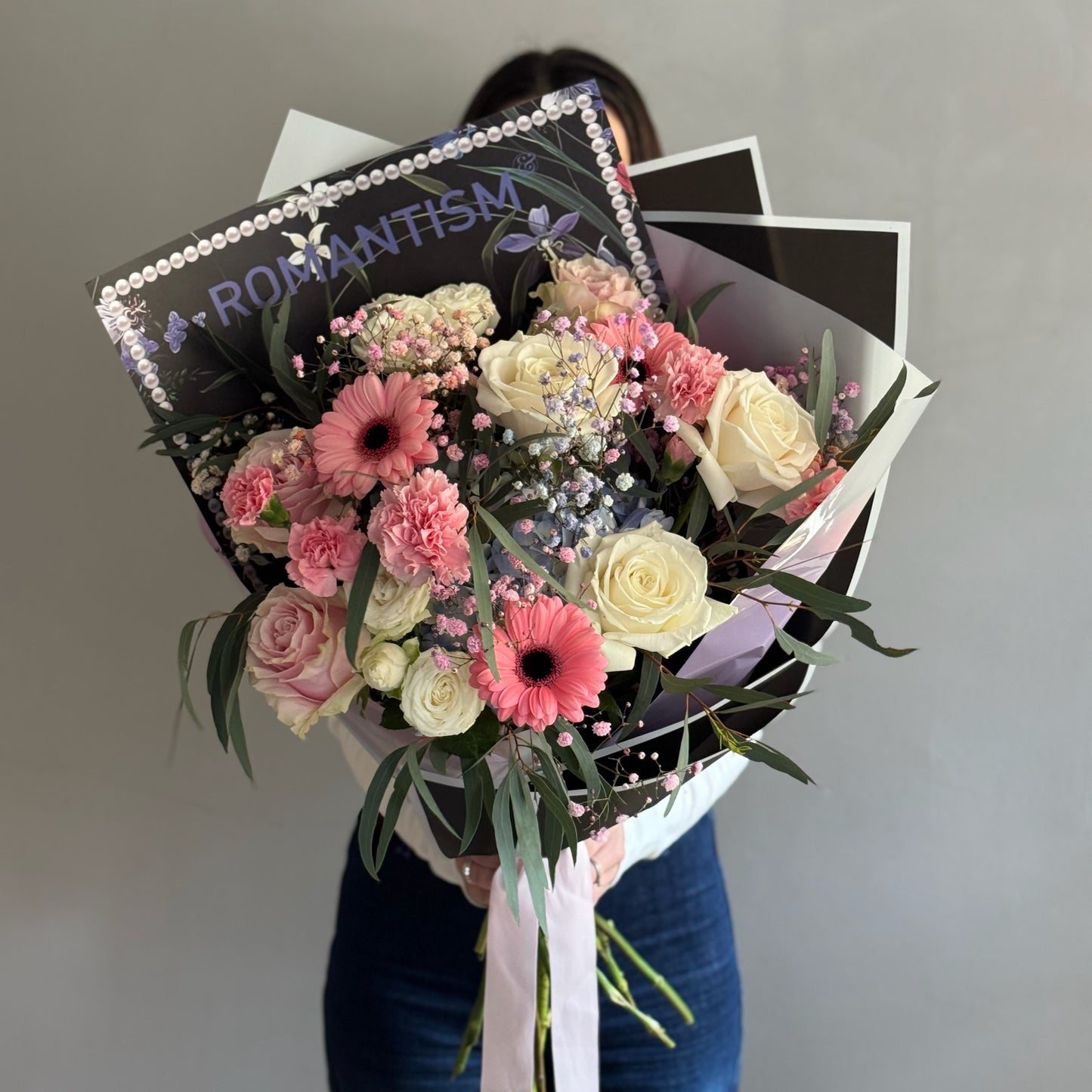 Bouquet of pink flowers with black wrapping paper held by person on grey background 