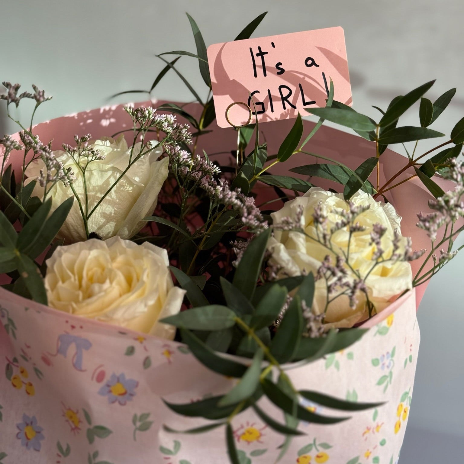 Bouquet of flowers with a 'It's a Girl' sign on floral-patterned paper.