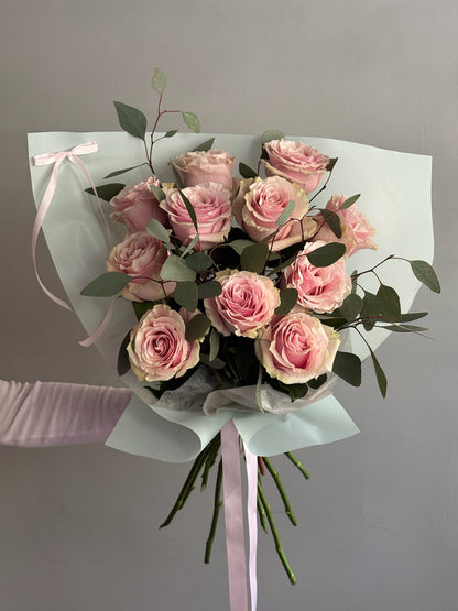 Bouquet of pink flowers wrapped in paper held by a person against a gray background