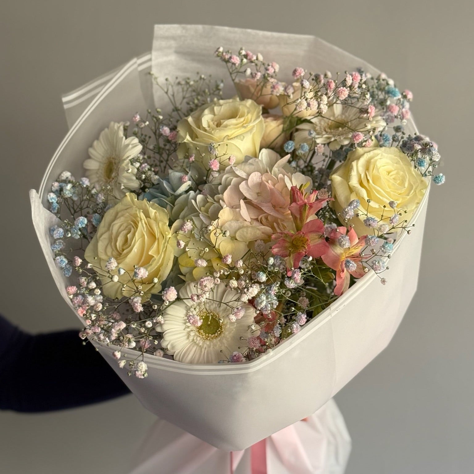 Bouquet of flowers wrapped in white paper with a pink ribbon on a neutral background