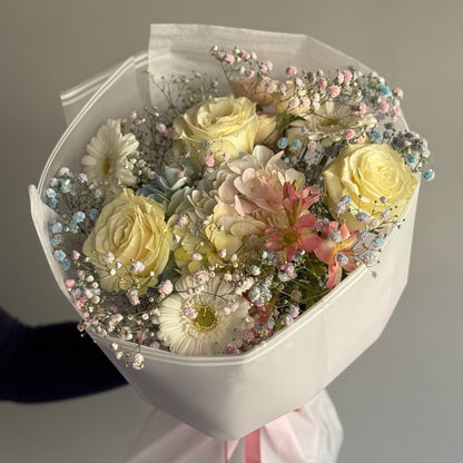 Bouquet of flowers wrapped in white paper with a pink ribbon on a neutral background