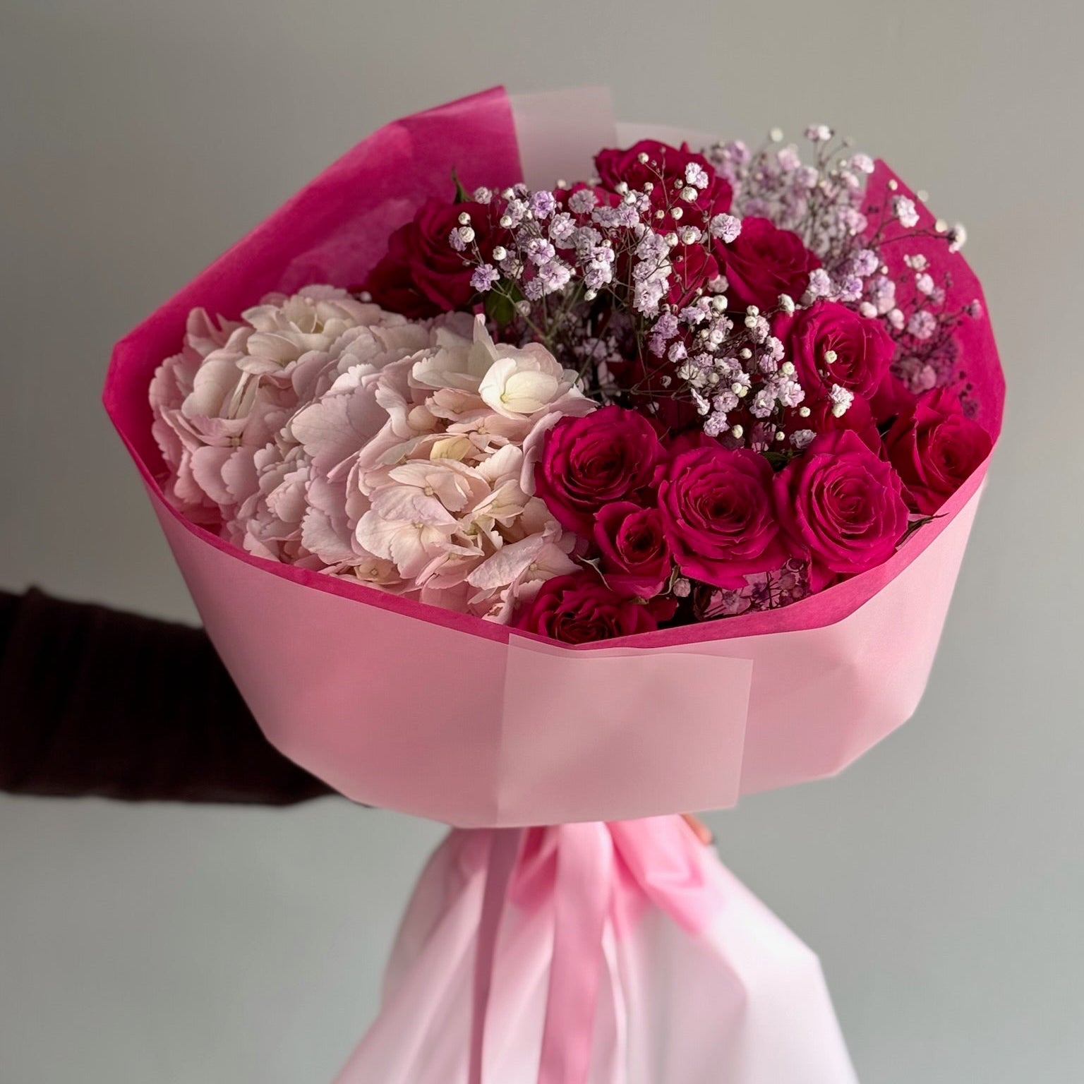 Bouquet of pink and red flowers wrapped in pink paper with a gray background