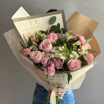 Big floral bouquet with colorful wrapping paper held by person on grey background 