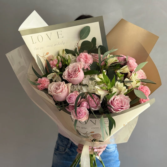 Big floral bouquet with colorful wrapping paper held by person on grey background 
